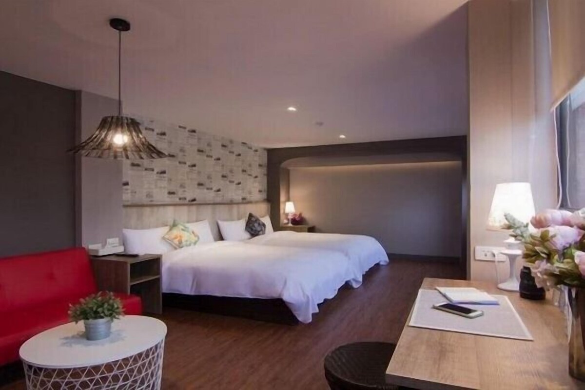 A modern hotel room with a bed, a red sofa, a small round table, and a decorative lamp.