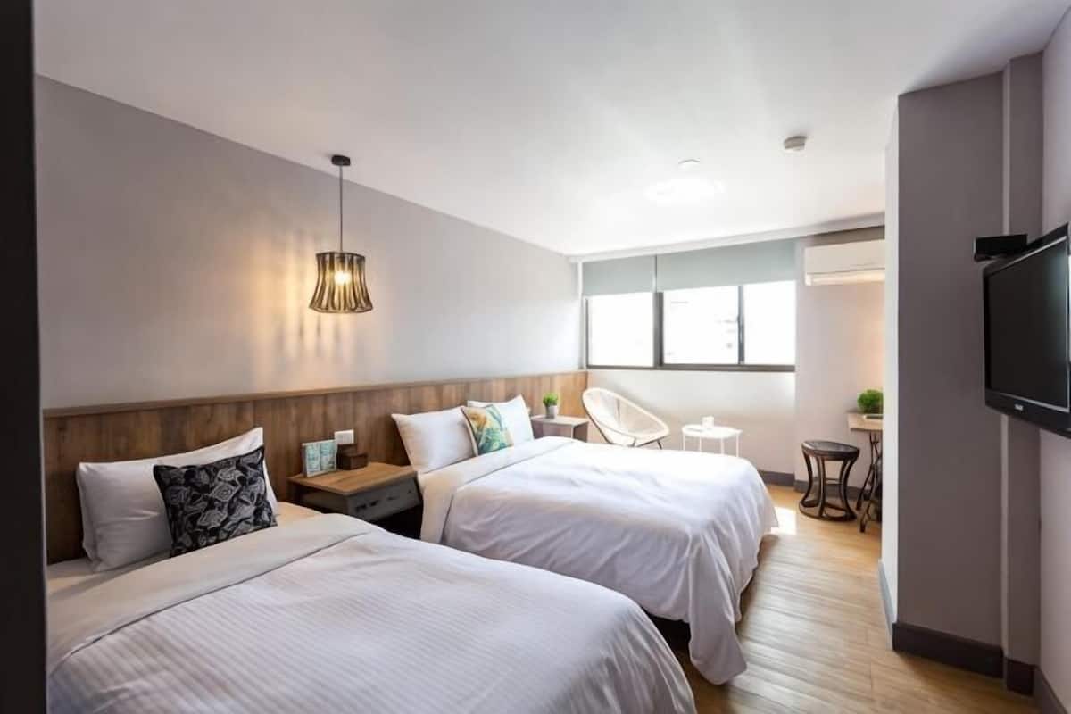 Quarto de hotel com duas camas, televisão, escrivaninha e uma cadeira.