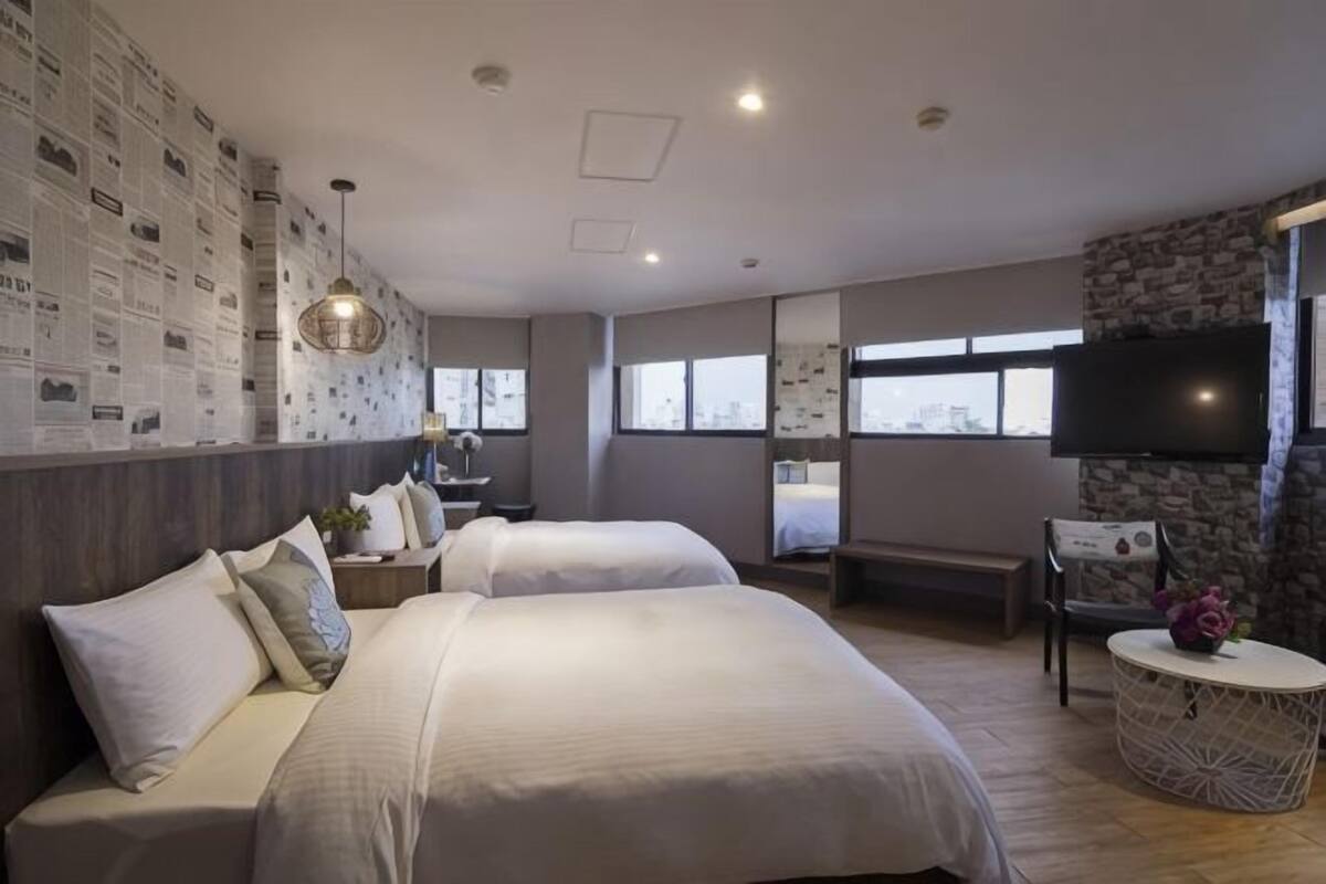 A hotel room with two beds, a TV, a desk, and a stone accent wall.