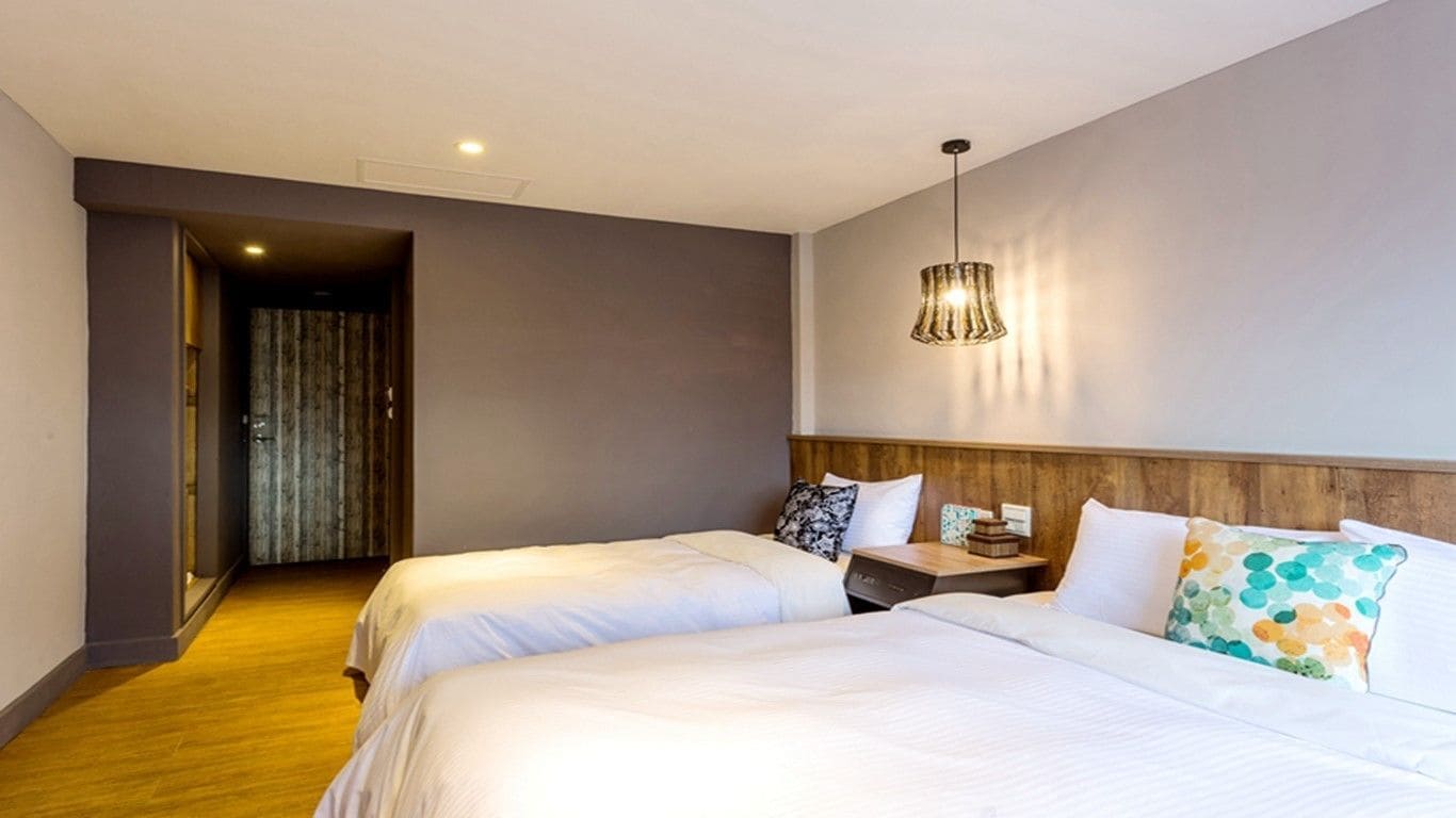 A hotel room with two beds, a wooden headboard, a nightstand, and a hanging light fixture.