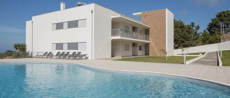 Un edificio moderno de dos pisos con piscina, un área exterior cubierta y una escalera que conduce a un balcón.