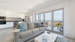 Een moderne woonkamer met een bank, een bijzettafeltje en uitzicht op zee door grote ramen.