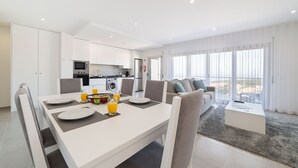 Een moderne woonkamer met een eethoek, keuken en grote ramen.