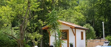 A small house with a tiled roof, surrounded by lush greenery and a swimming pool.