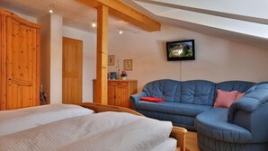A bedroom with two beds, wooden wardrobes, a blue sofa, and a television on the wall.