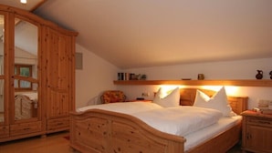 Una cama de madera con ropa de cama blanca en una habitación con techo inclinado y muebles de madera.