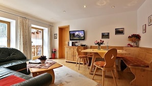 Una sala de estar acogedora con un sofá, una mesa de comedor con sillas, un televisor montado en la pared y una cocina con armarios de madera.