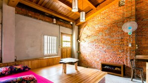 Una habitación con un banco de madera, una cama con ropa de cama floral, una pared de ladrillo y un ventilador.