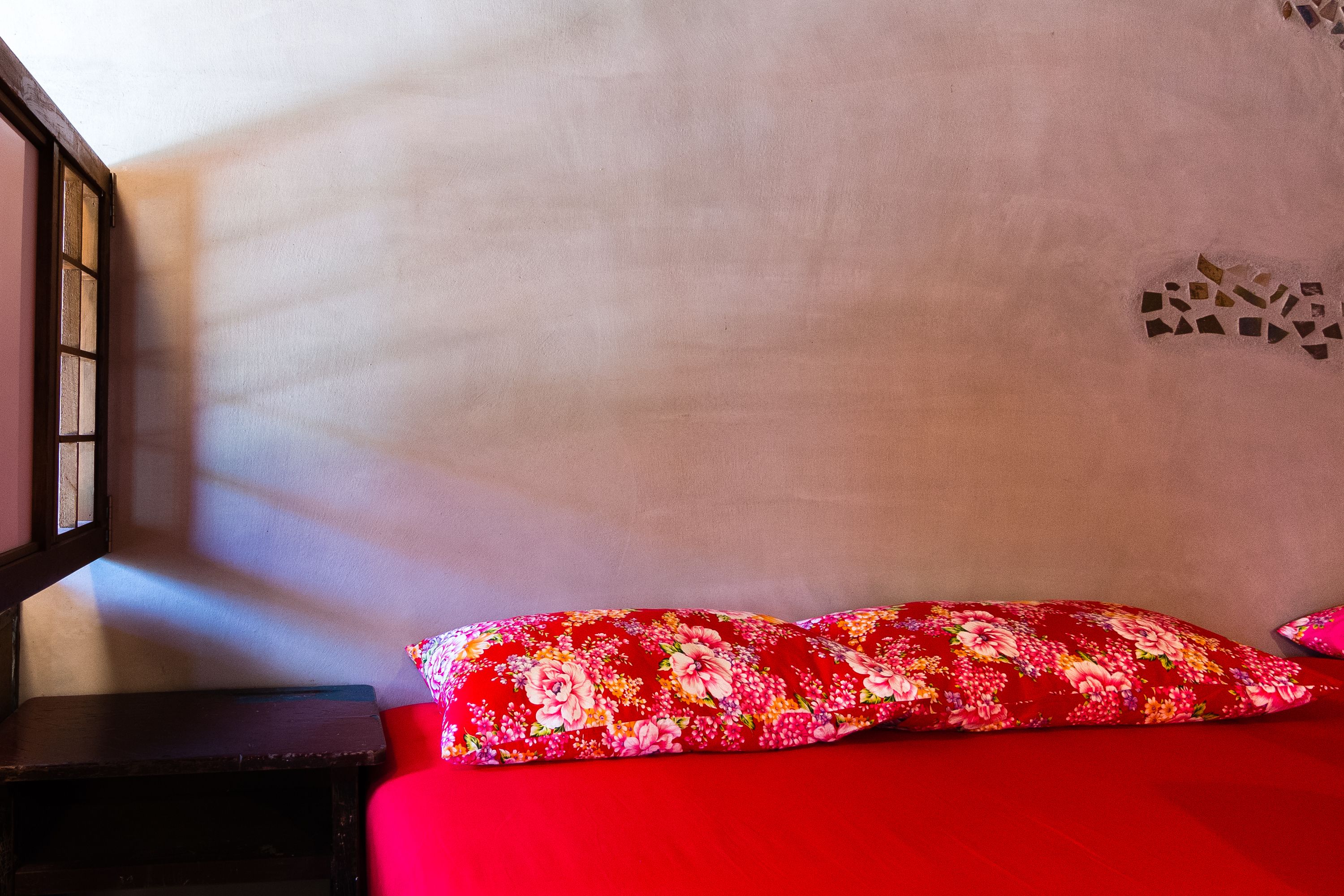 A room with a red bedspread, a wooden nightstand, and a wall with a mosaic design.
