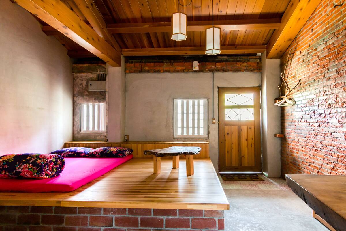 Um quarto com um banco de madeira, um tapete vermelho e uma parede de tijolos.