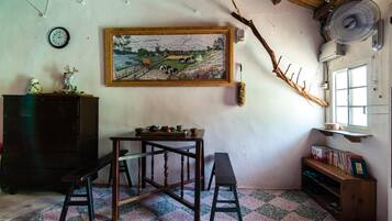 Une pièce avec une table en bois, des bancs, une horloge, un tableau encadré, un ventilateur et une fenêtre.