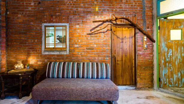 Una habitación acogedora con pared de ladrillo, puerta de madera, un banco y una pequeña mesa con un adorno.
