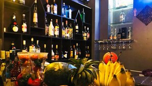 A bar area with shelves of liquor bottles, a fruit display including pineapple and bananas, and a glass with a red label. - Tonle Khmer Guesthouse (Phnom Penh)