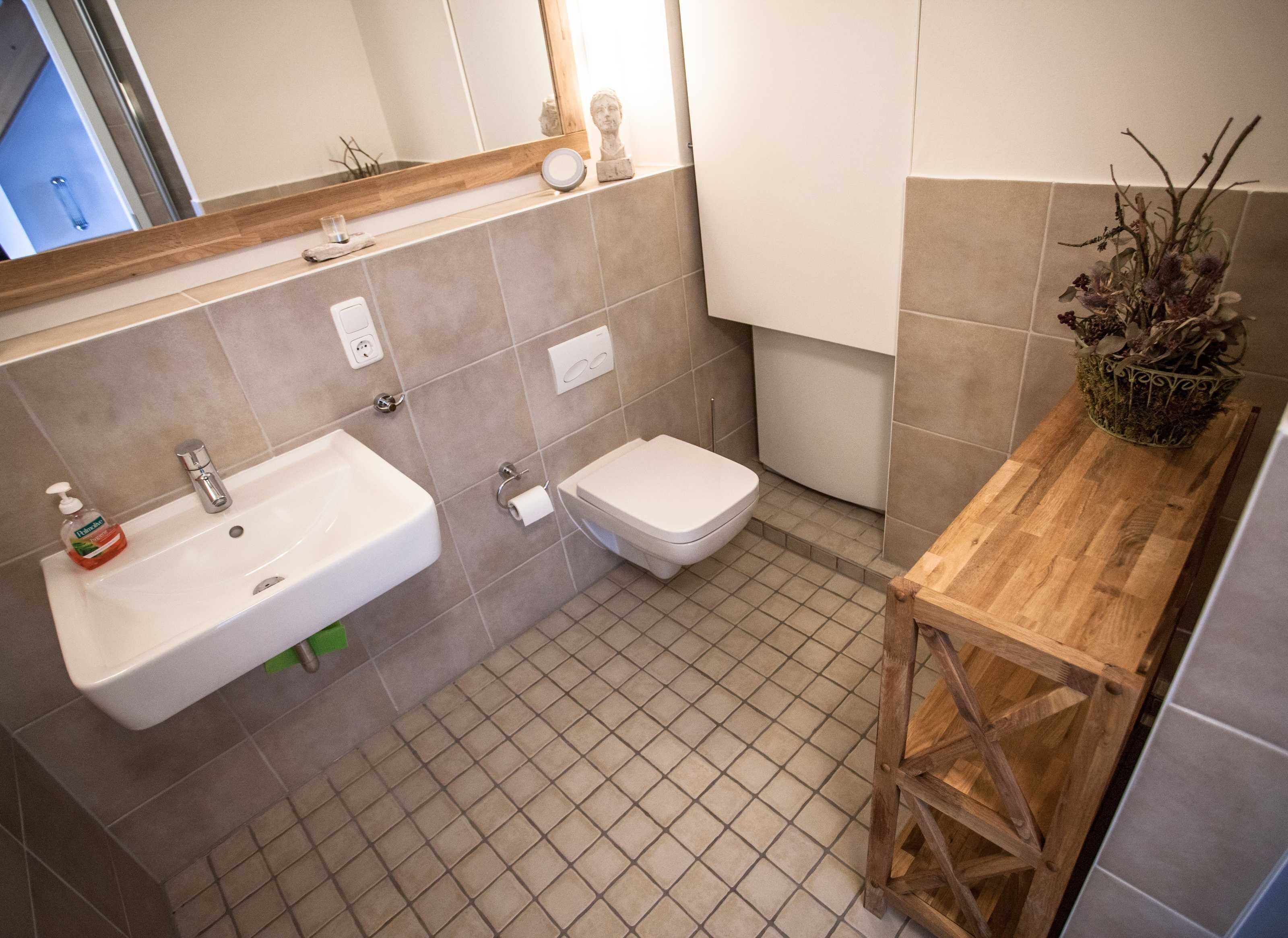 A bathroom with a sink, toilet, and a wooden vanity with a vase of dried flowers.