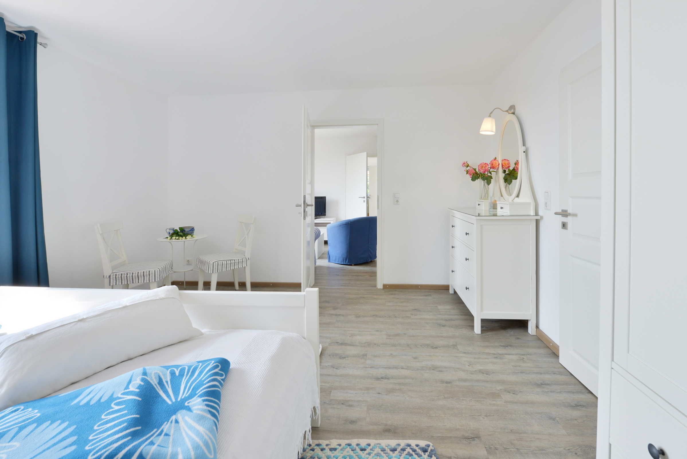 A bedroom with a bed, a dresser, a mirror, and a small table with flowers.