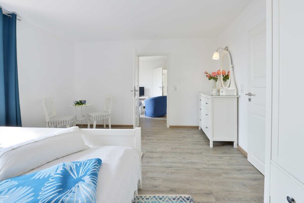 A bedroom with a bed, a dresser, a mirror, and a small table with flowers.