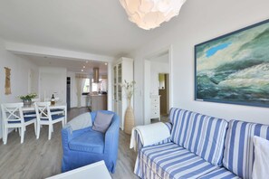 A modern living room with a blue sofa, a striped sofa, and a dining area with white chairs and a table.