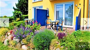A yellow building with a blue door, outdoor seating, and a garden with various plants.