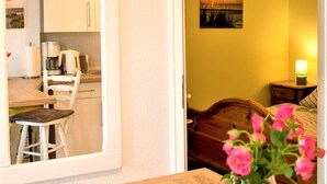 A room with a wooden table, a vase with flowers, a bed, a nightstand, and a painting on the wall.