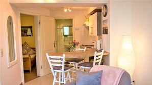 A cozy living room with a sofa, a dining table with chairs, and a kitchen area visible through an open door.