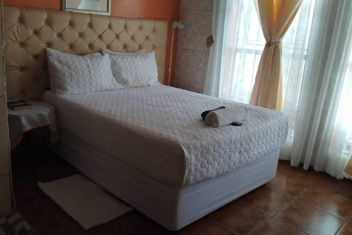 A neatly made bed with a tufted headboard, a bedside table with a lamp, and a window with curtains.