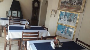 A dining area with tables covered in white tablecloths and blue placemats, wooden chairs, and a wall-mounted clock. - Diphororo Guest House (Moses Kotane)