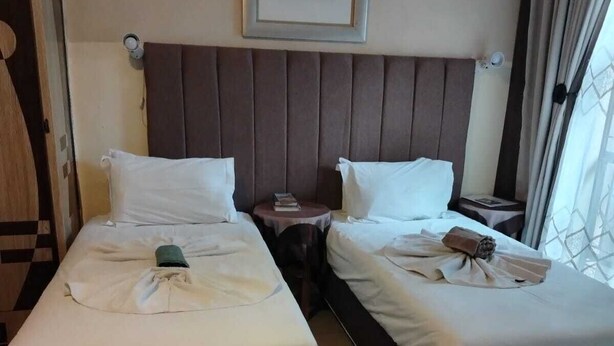 A hotel room with two beds, a headboard, a framed picture, and a window with curtains. - Diphororo Guest House (Moses Kotane)