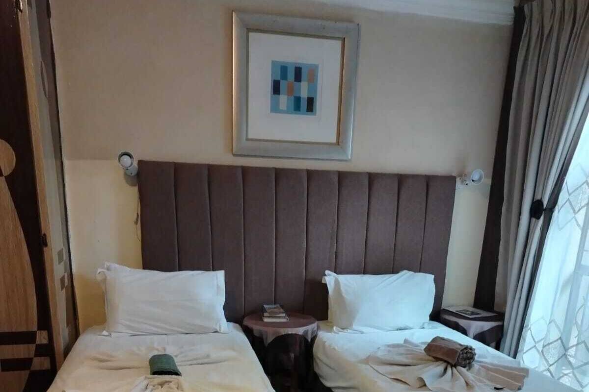 A hotel room with two beds, a headboard, a framed picture, and a window with curtains.