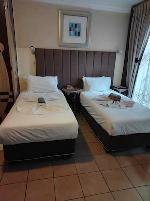 Ein Hotelzimmer mit zwei Betten, einem Kopfteil, einem gerahmten Bild und einem Fenster mit Vorhängen.