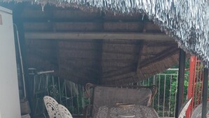 A covered patio area with a metal table and white chairs, a refrigerator, and a thatched roof. - Diphororo Guest House (Moses Kotane)