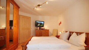 A bedroom with a wooden bed, a television on a stand, a wardrobe, and a mirror. - Vacation apartment Hoher Göll, 2-3 persons, 60 sqm, shower/WC, balcony, TV, W-LAN (Ramsau bei Berchtesgaden)