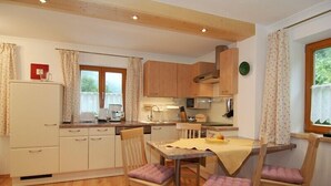 A compact kitchen with wooden cabinets, a dining table with chairs, and a window with curtains. - Vacation apartment Hoher Göll, 2-3 persons, 60 sqm, shower/WC, balcony, TV, W-LAN (Ramsau bei Berchtesgaden)