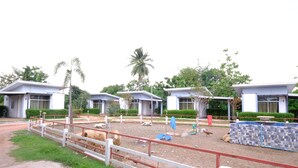 A fenced outdoor area with a dirt ground, surrounded by modern buildings with flat roofs and large windows.