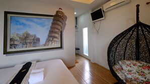 A hotel room with a bed, a framed picture of the Leaning Tower of Pisa, a black hanging chair, and an air conditioning unit.
