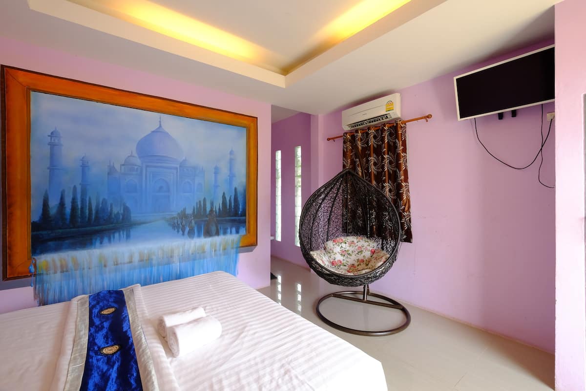 A hotel room with a bed, a large painting of the Taj Mahal, a hanging chair, and an air conditioning unit.