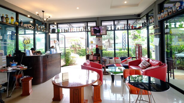 A hotel lobby with a reception desk, seating area with red and orange chairs, a round wooden table, and large windows offering a view of the outdoors.