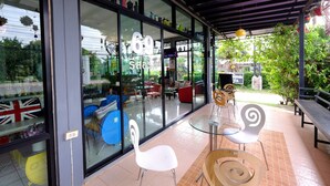 A modern cafe with large windows, outdoor seating, and a variety of chairs and tables.