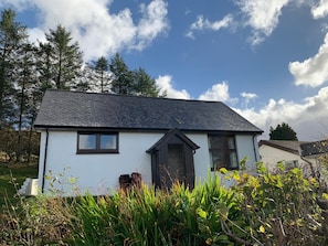 A single-story house with a dark roof and white walls, surrounded by greenery and trees. - Loch Eyre Cottage (Skeabost)