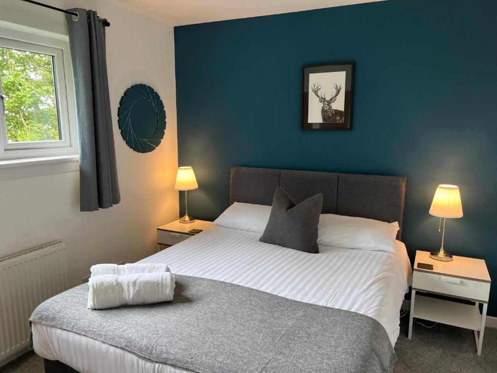 Un dormitorio con una cama, dos mesitas de noche, un ventanal con cortinas, una obra de arte en la pared y un radiador.
