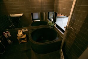 A bathroom with a large bathtub, a small toilet, and a window.