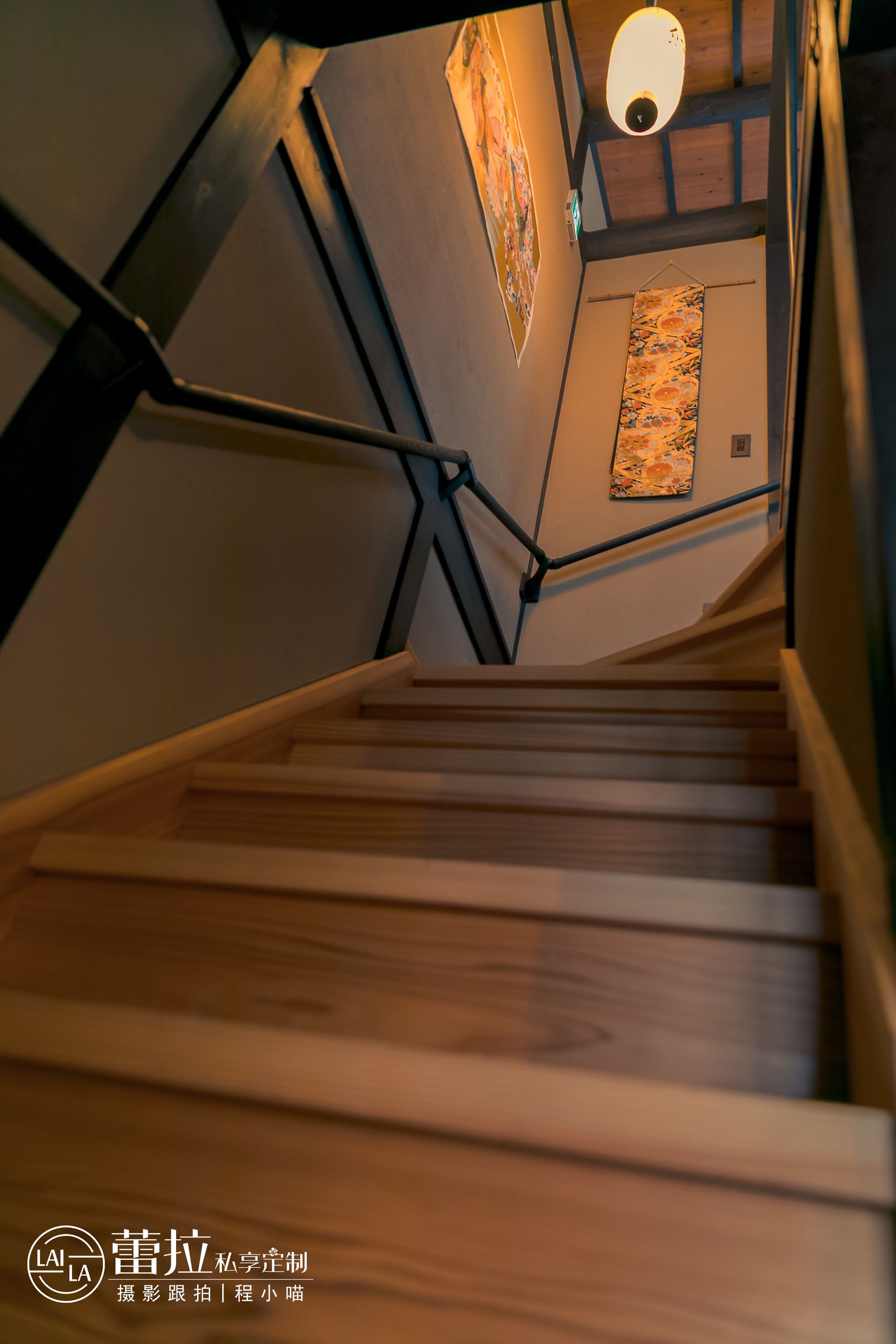 Una escalera de madera con barandillas de metal que lleva a una habitación con un tapiz de pared estampado.