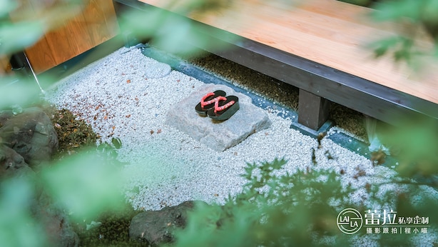 A wooden bench with a stone slab in the center, surrounded by white pebbles and greenery. - Kyo-Machiya YululY (Kyoto)