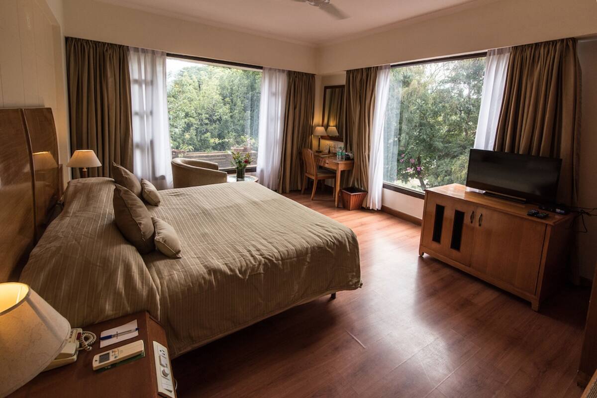 Hotellihuone, jossa on suuri sänky, työpöytä tuolilla, televisio ja näkymä ulos.