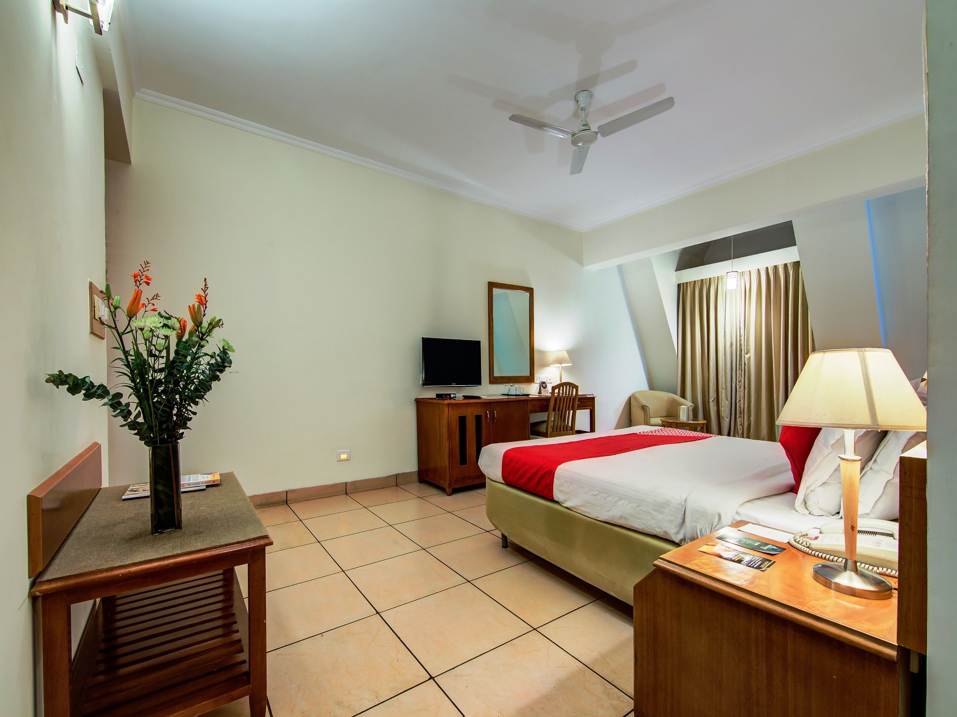 A hotel room with a bed, desk, chair, TV, and a ceiling fan.