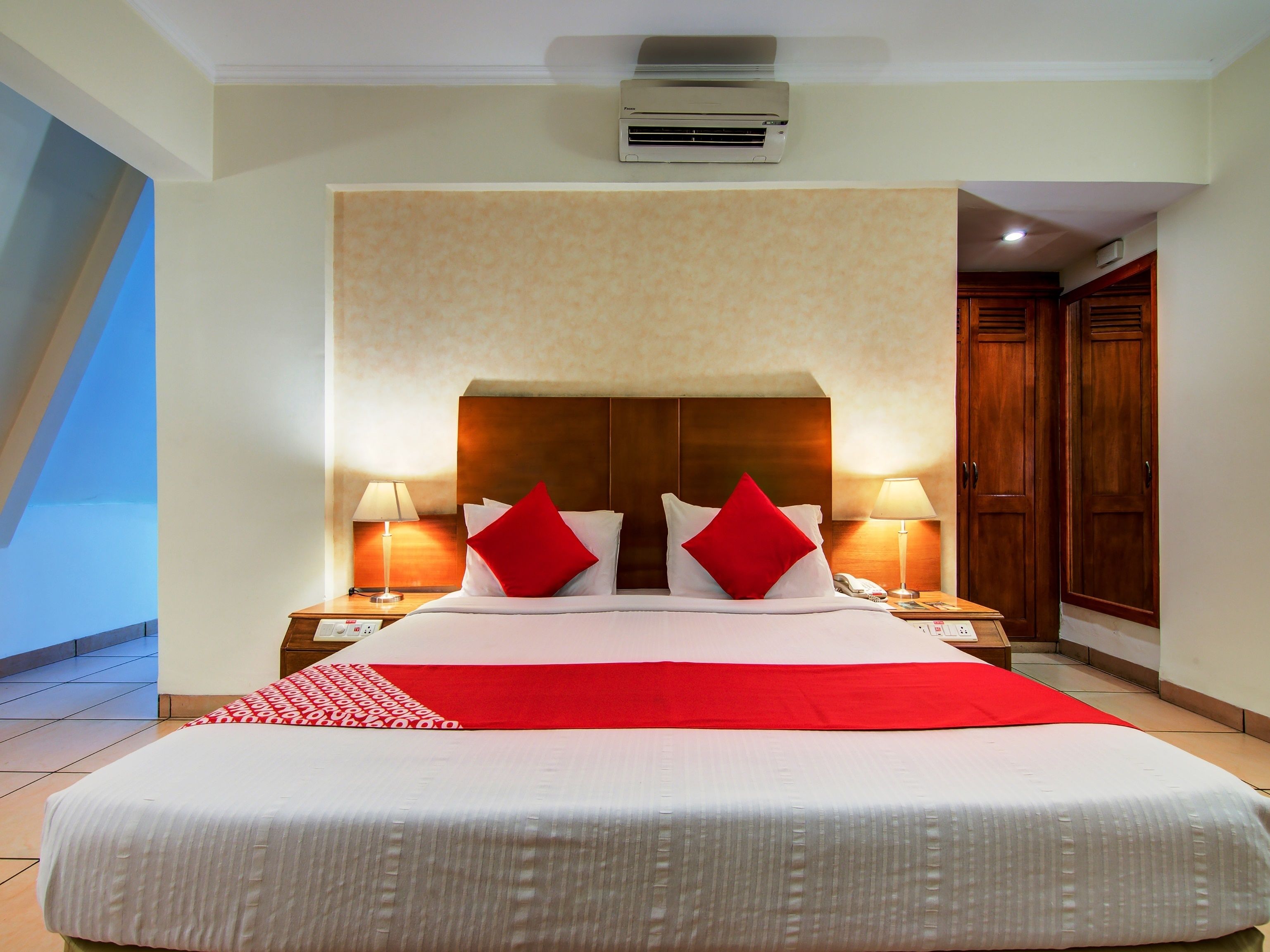 Una habitación de hotel con una cama grande, dos mesitas de noche, una manta roja y un cabecero de madera.