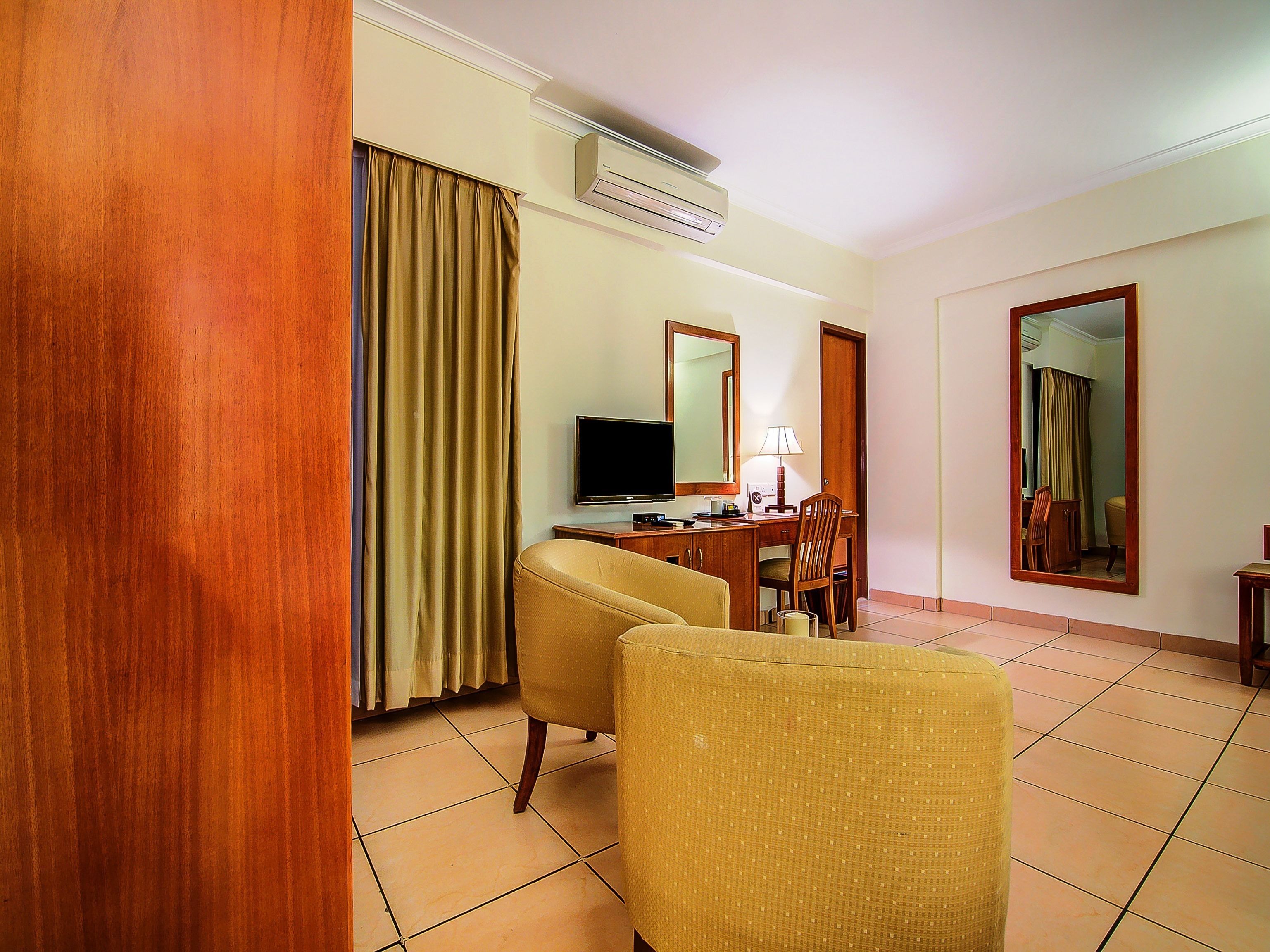 A hotel room with a wooden floor, a desk with a computer, a chair, a television, and a mirror.