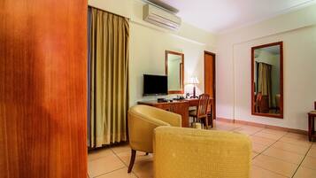 A hotel room with a wooden floor, a desk with a computer, a chair, a television, and a mirror.