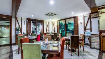 Un restaurante con techo alto, vigas de madera y un ventanal con vistas a un edificio histórico. Las mesas están preparadas con platos, vasos y cubiertos.