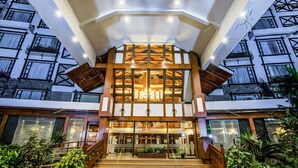 A multi-story hotel with a central atrium, wooden staircase, and potted plants. - Sai Vishram Business Hotel (Anekal)
