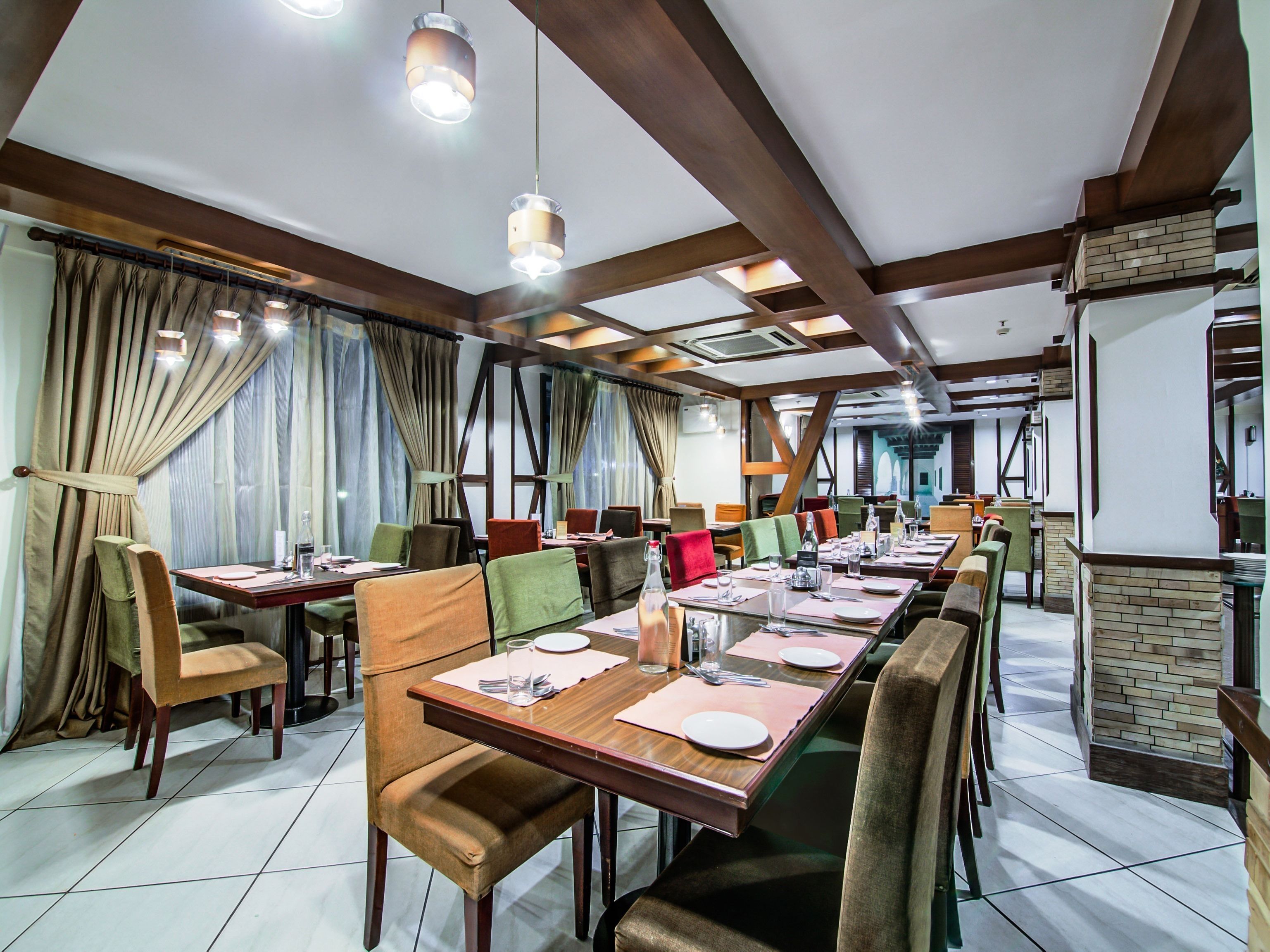 A restaurant with long tables, chairs, and hanging pendant lights.